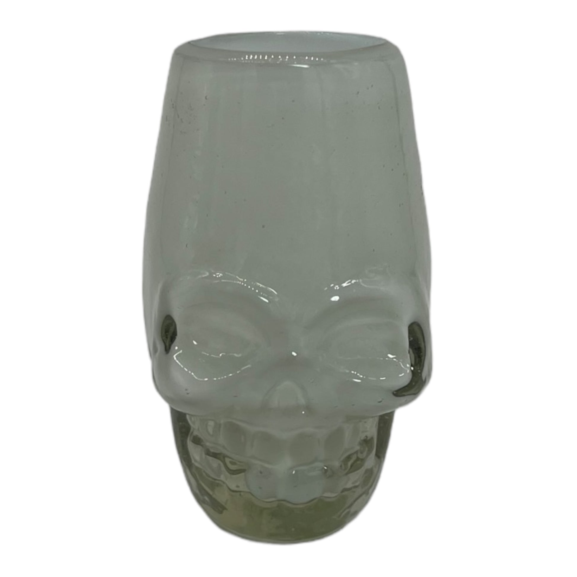 handblown Mexican shot glass, shaped like a skull and crafted from eco-friendly recycled glass. The glass is translucent with a subtle greenish tint and holds approximately 2 fluid ounces.