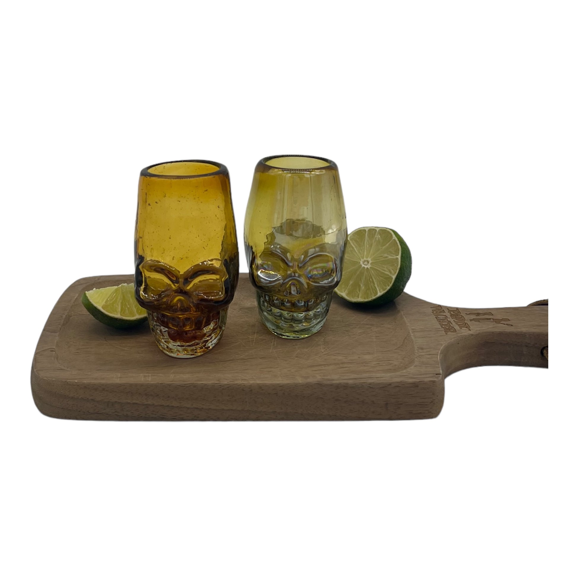 handblown Mexican shot glass, shaped like a skull and crafted from eco-friendly recycled glass. It features a gradient color scheme transitioning from dark at the base to a lighter amber at the top. The glass holds approximately 2 fluid ounces.