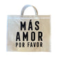 beige tote bag with white handles and "MÁS AMOR POR FAVOR" in large black letters.