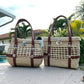 Two woven palm handbags with brown vegan leather straps and silver clasps, one rounded and one rectangular