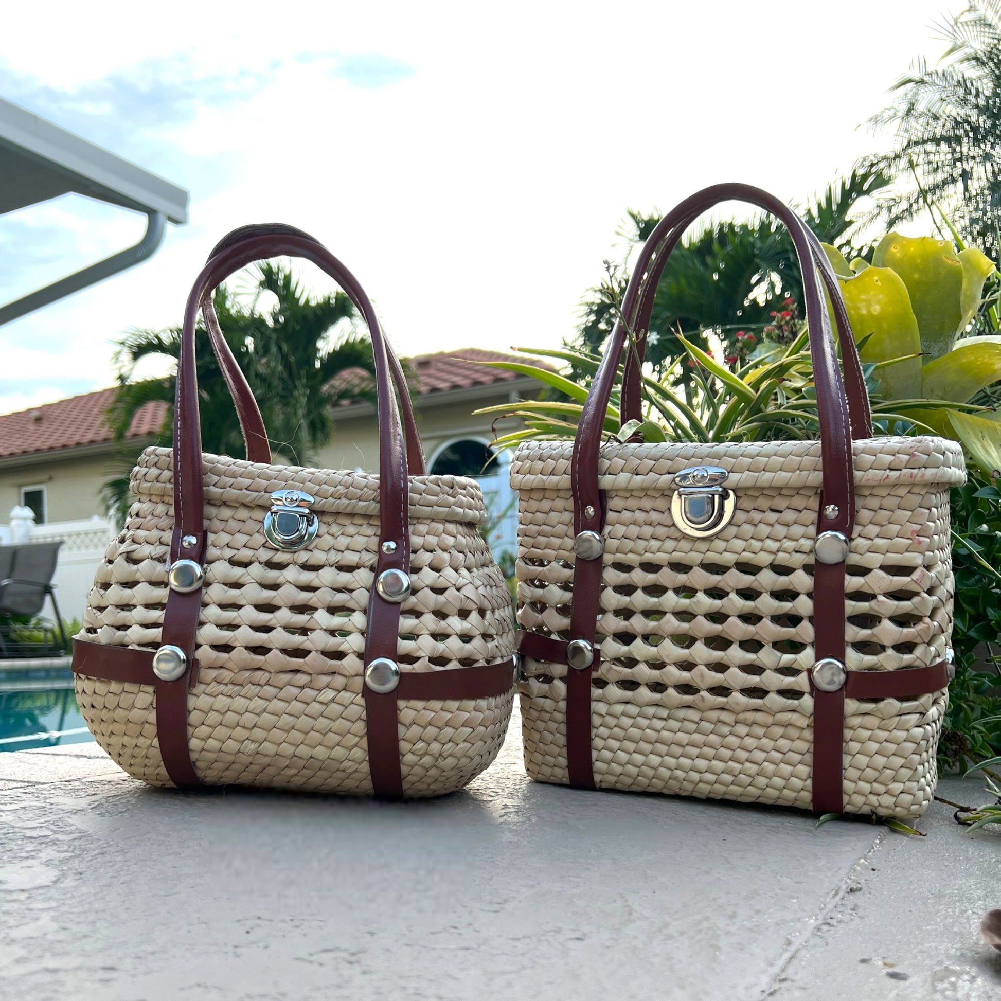 Two woven palm handbags with brown vegan leather straps and silver clasps, one rounded and one rectangular