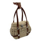 woven palm handbag with brown vegan leather straps, a silver clasp, and a rounded shape, shown being held.