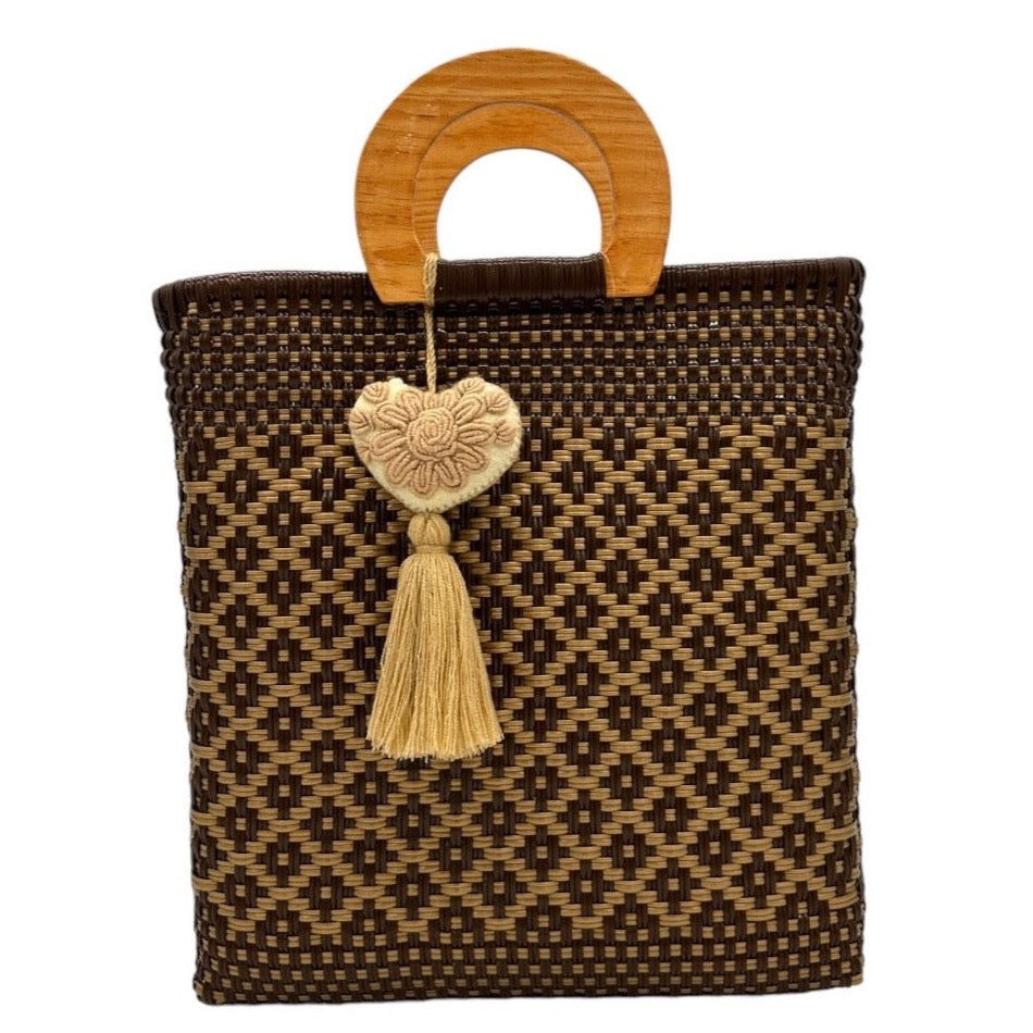 dark brown woven tote bag made of recycled plastic with a wooden circular handle. The bag features a geometric pattern in light brown and is adorned with a  heart-shaped charm with a tassel.