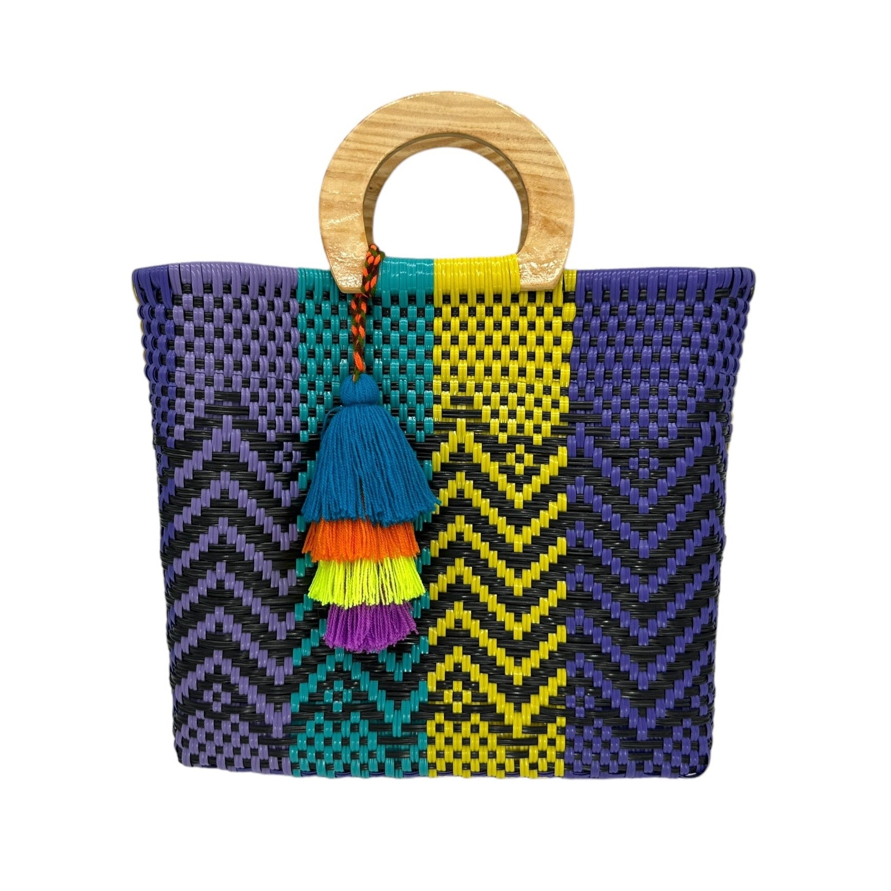 woven tote bag made of recycled plastic with a wooden circular handle. The bag features a vibrant pattern in purple, blue, yellow, and black, with zigzag and checkered designs. It is adorned with a tassel charm.