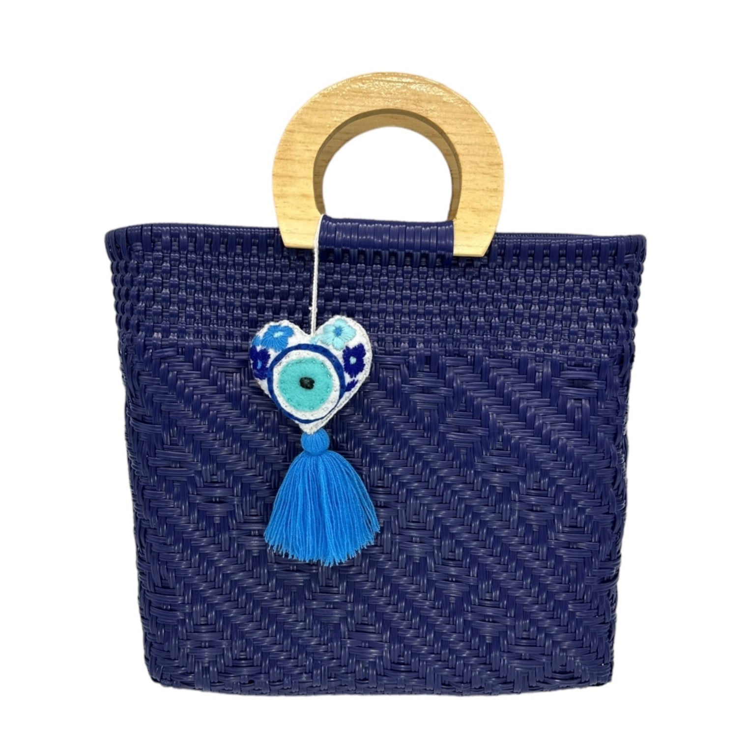 dark blue woven tote bag made of recycled plastic, featuring a wooden circular handle. The bag is adorned heart-shaped charm with a tassel.