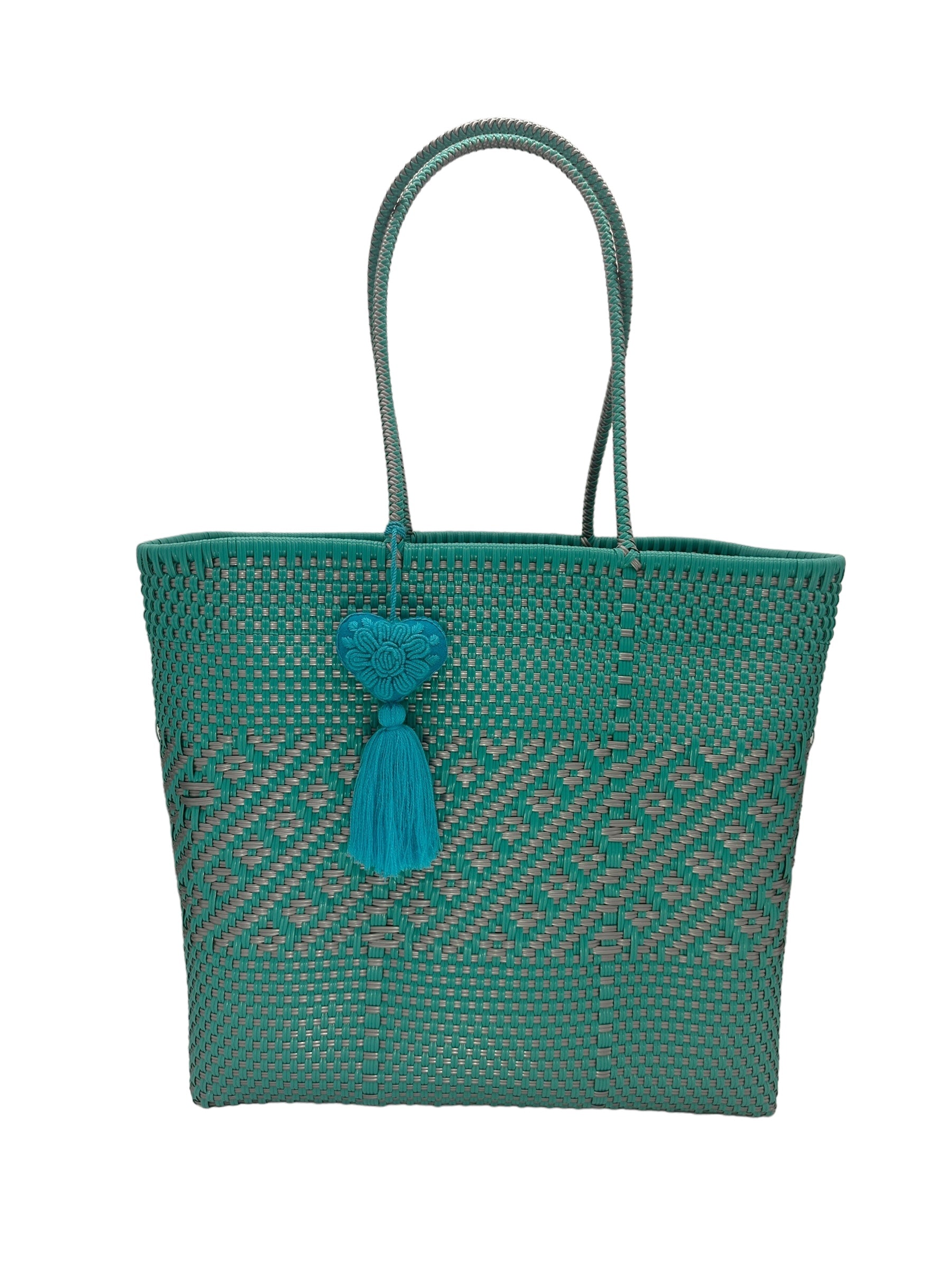 green tote bag with a woven pattern, two handles, and a small heart and tassel attached.