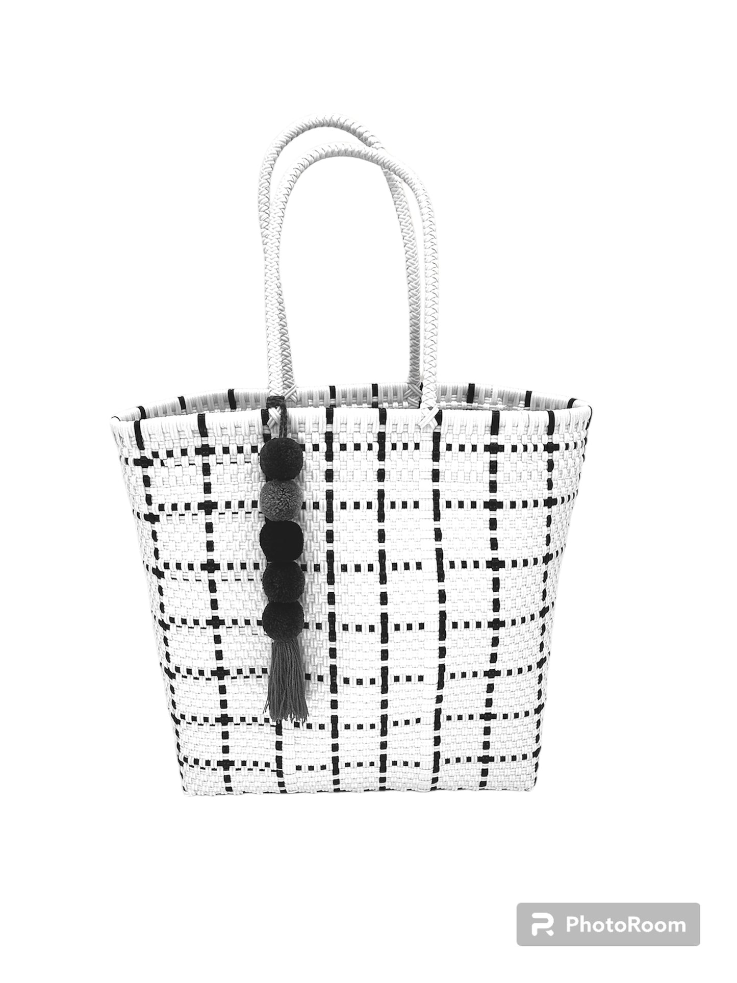 woven white handbag with black checkered patterns, featuring two handles and pom-pom charm with tassel.