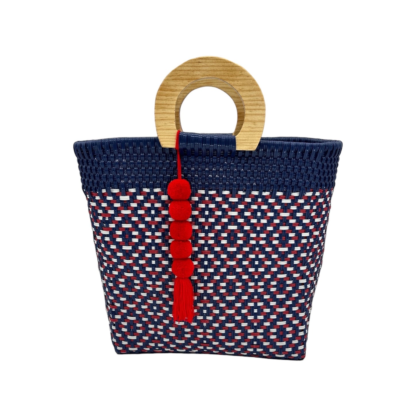 woven tote bag made of recycled plastic with a wooden circular handle. The bag features geometric patterns in red, white & blue. It is adorned with a coordinating pompon