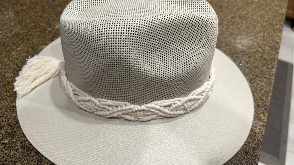 white hat with a wide brim and a braided rope band, topped with a small tassel, displayed on a granite countertop.