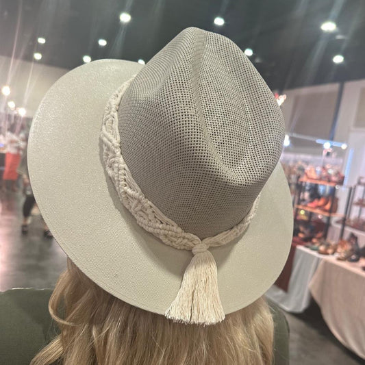 white hat with a wide brim and a braided rope band, topped with a small tassel, displayed on a granite countertop.