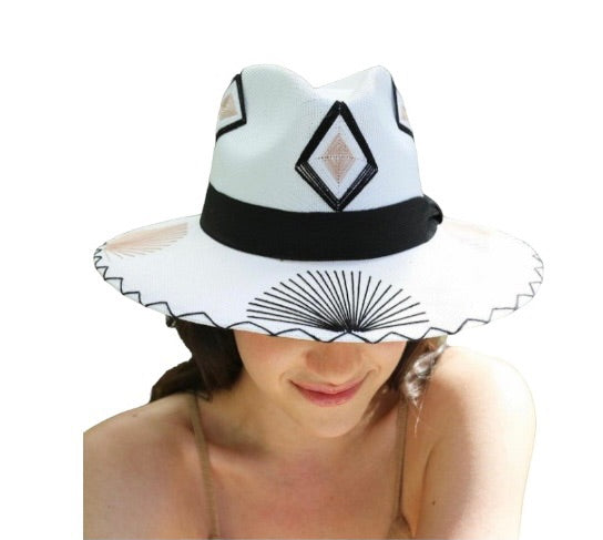 white Fedora hat with black and gold hand-stitched tribal designs. The hat features a black band and diamond-shaped patterns on the crown, with a wide brim adorned with additional stitching.