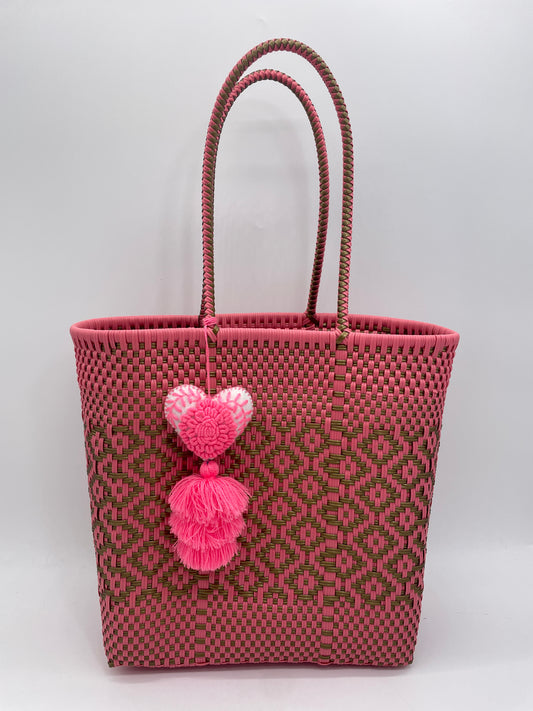 pink woven handbag with green accents, featuring a pair of looped handles and adorned with a heart-shaped tassel charm.