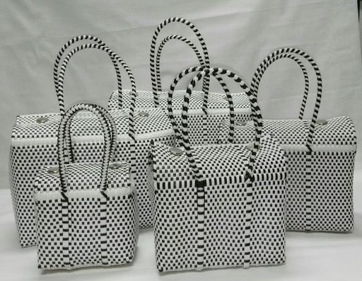 collection of handcrafted handbags made from 100% recycled plastic, featuring a uniform black and white checkerboard pattern. These bags come in various sizes, each with matching patterned handles, ideal for travel, beach days, boating, or other outdoor activities. The design is visually striking, combining environmental consciousness with practical functionality.