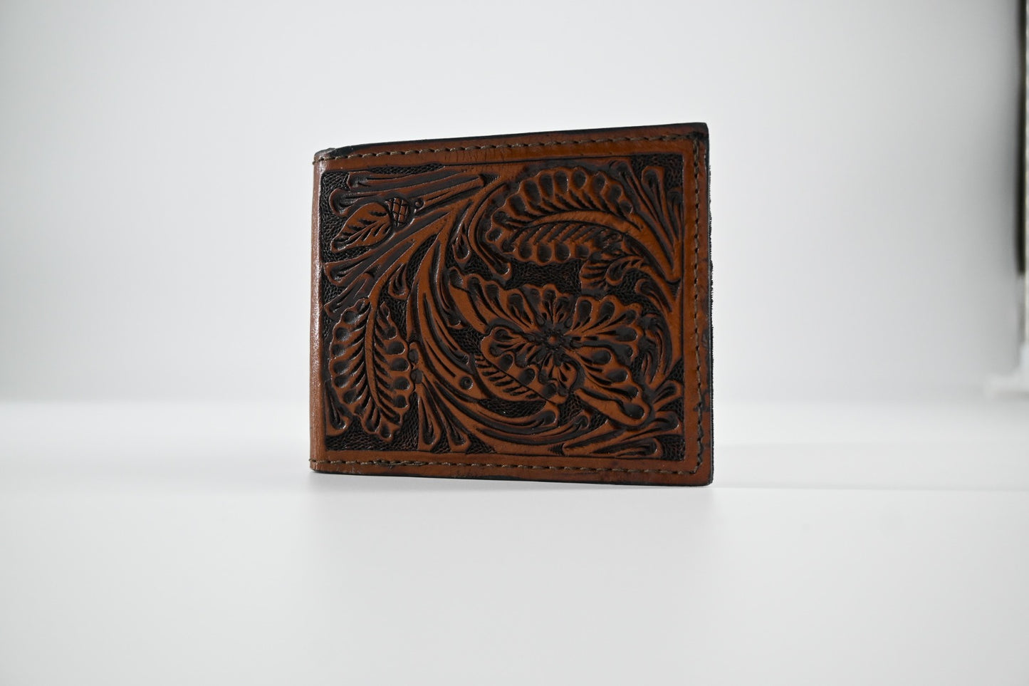 brown leather bi-fold wallet with intricate hand-carved floral detailing.