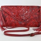 red leather clutch with intricate floral carvings, long side tassels, and a matching braided strap. It has a snap front closure.