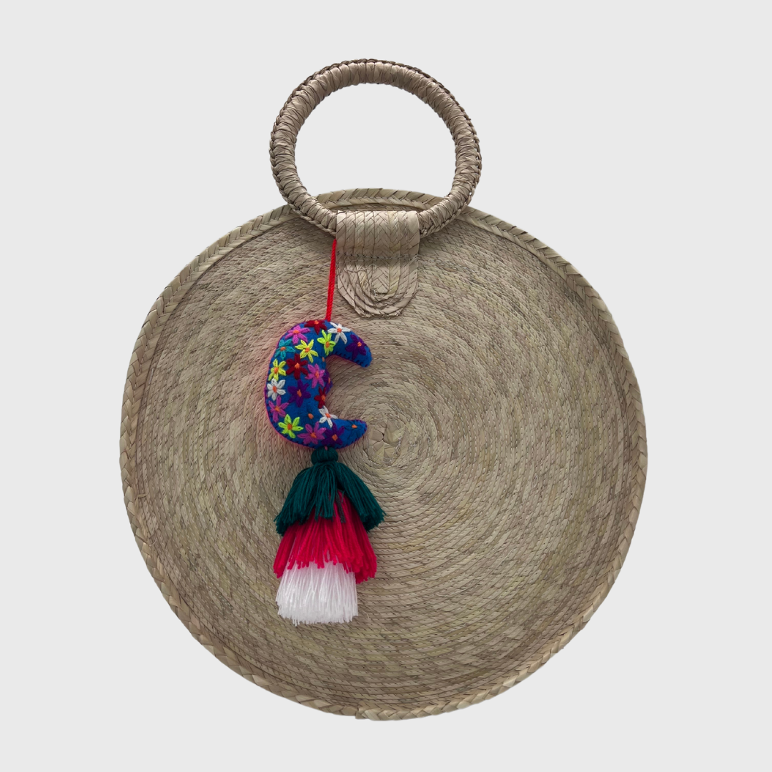 featuring a colorful crescent moon ornament with multicolored embroidered flowers and a tassel in green, red, and white hanging from it.