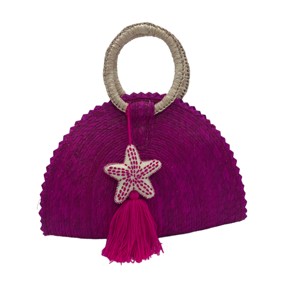 bright fuchsia woven palm handbag with a round handle wrapped in a natural material. The bag is adorned with a starfish decoration and a matching tassel hanging from the center.