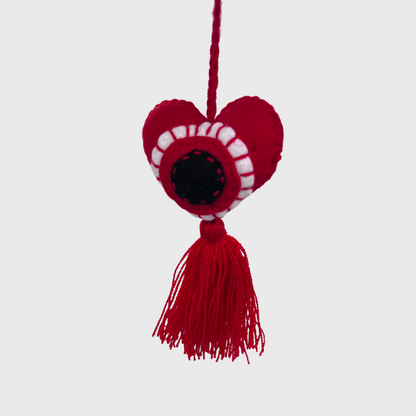 red heart-shaped ornament with white and black stitched details, featuring a red tassel hanging from the bottom.