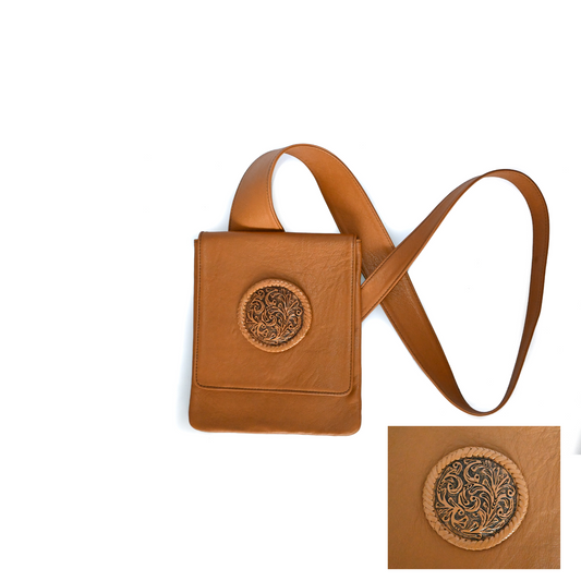 Honey leather crossbody bag with an ergonomic strap. It features a circular medallion design with hand-braided leather detailing on the front flap, which has a snap closure. The bag is lined with suede.