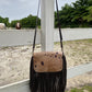 brown leather hobo bag with long fringe and a cowhide flap featuring dark spots. The bag has an adjustable shoulder strap