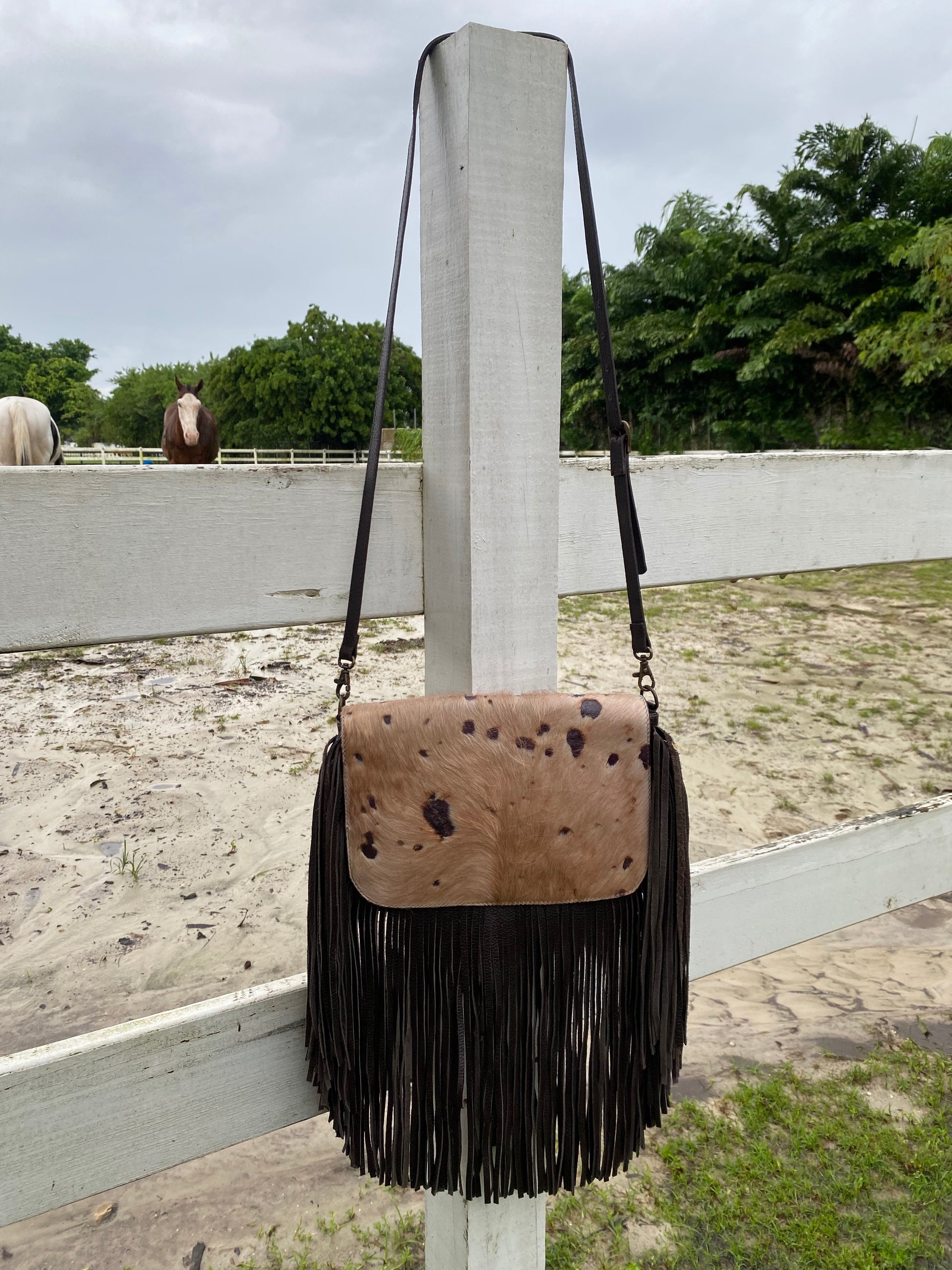 brown leather hobo bag with long fringe and a cowhide flap featuring dark spots. The bag has an adjustable shoulder strap