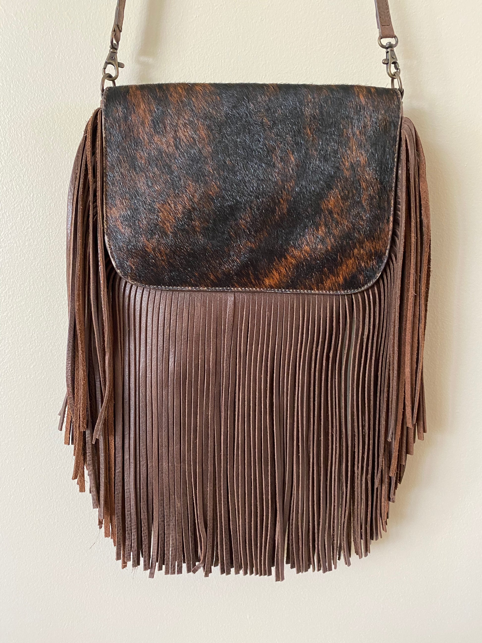 brown leather hobo bag with long fringe and a dark brown cowhide flap with black and orange speckles. The bag has an adjustable shoulder strap