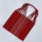handwoven tote bag featuring vibrant, multicolored stripes on a red background with intertwined straps