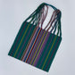 handwoven tote bag featuring vibrant, multicolored stripes on a dark green background with intertwined straps.