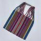 handwoven tote with purple, red, teal, olive green, and orange stripes on a taupe background, featuring multicolored braided straps.