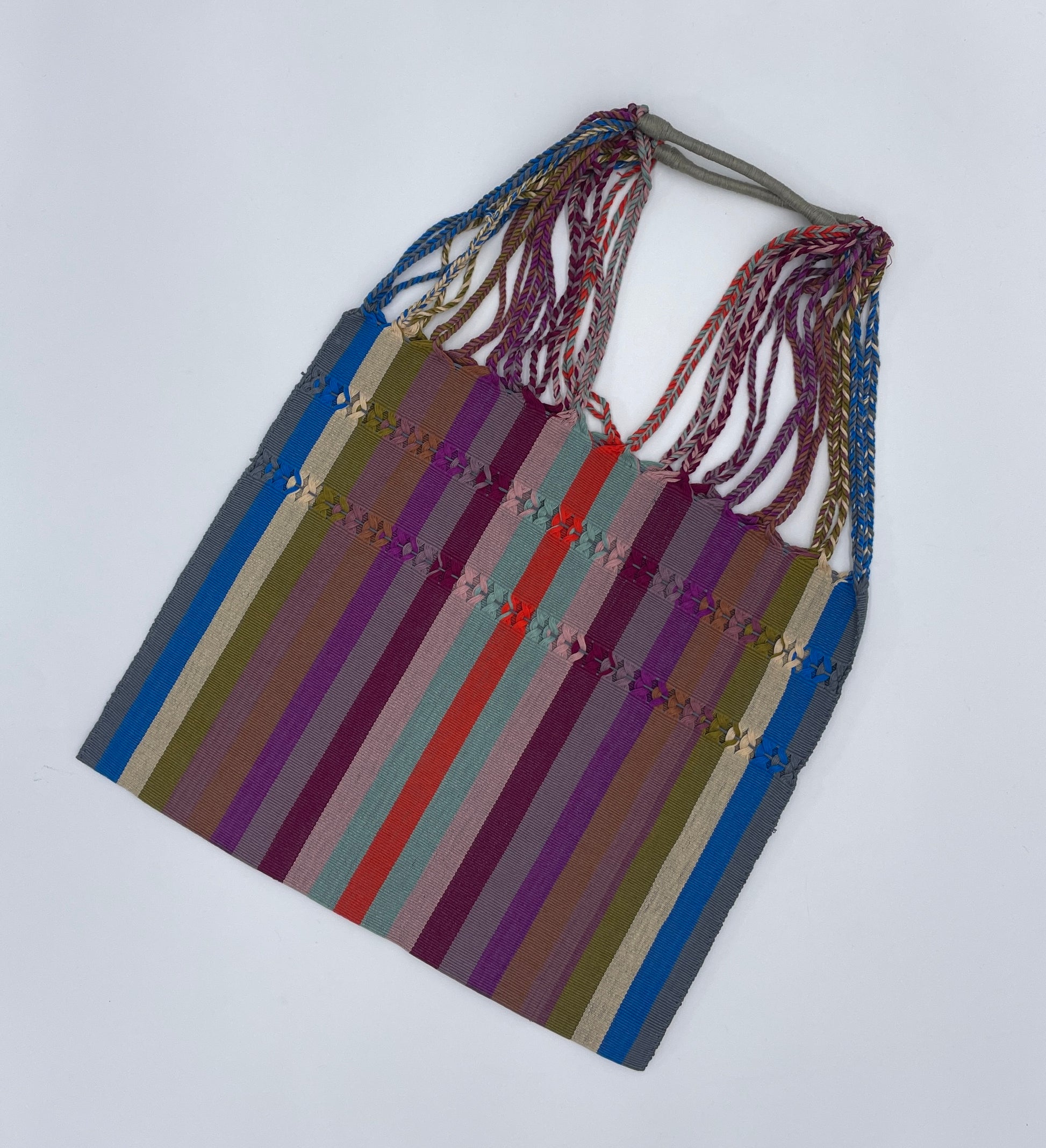 handwoven tote with purple, red, teal, olive green, and orange stripes on a taupe background, featuring multicolored braided straps.