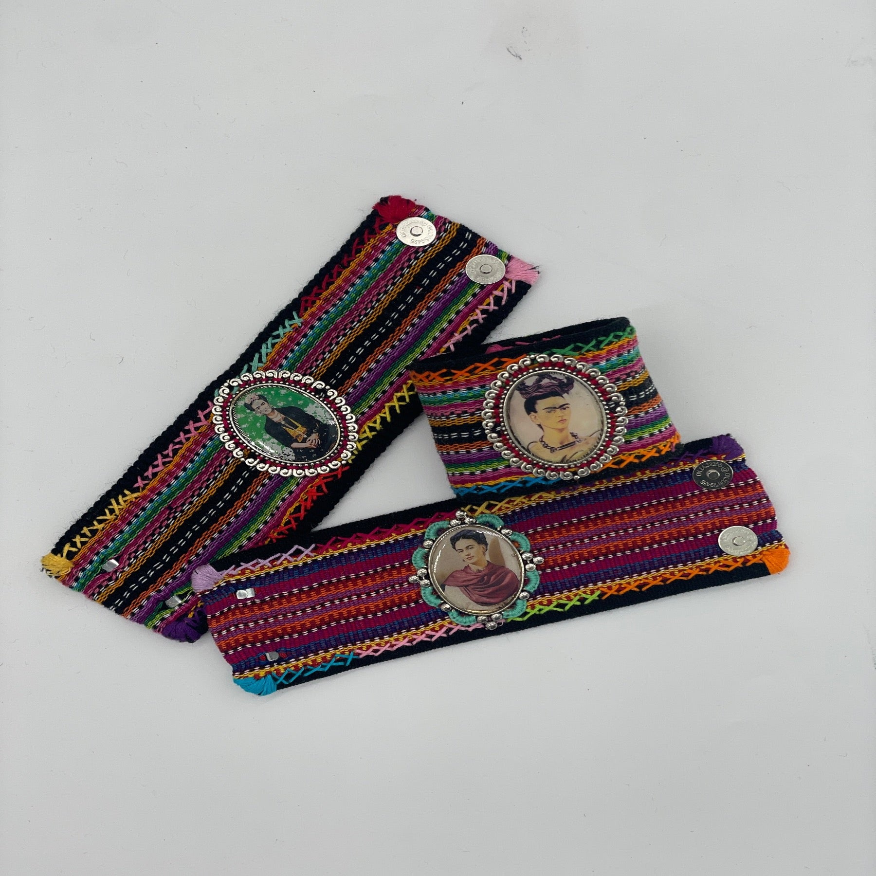 three colorful handwoven cuff bracelets, each featuring a central framed image: one of The Virgin Mary and two of Frida Kahlo. The bracelets are richly patterned with vibrant multicolored threads and close with magnetic snaps.