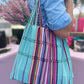 handwoven tote bag with colorful vibrant stripes and intertwined straps. The bag is large and suitable for various uses such as trips to the farmer's market or beach.