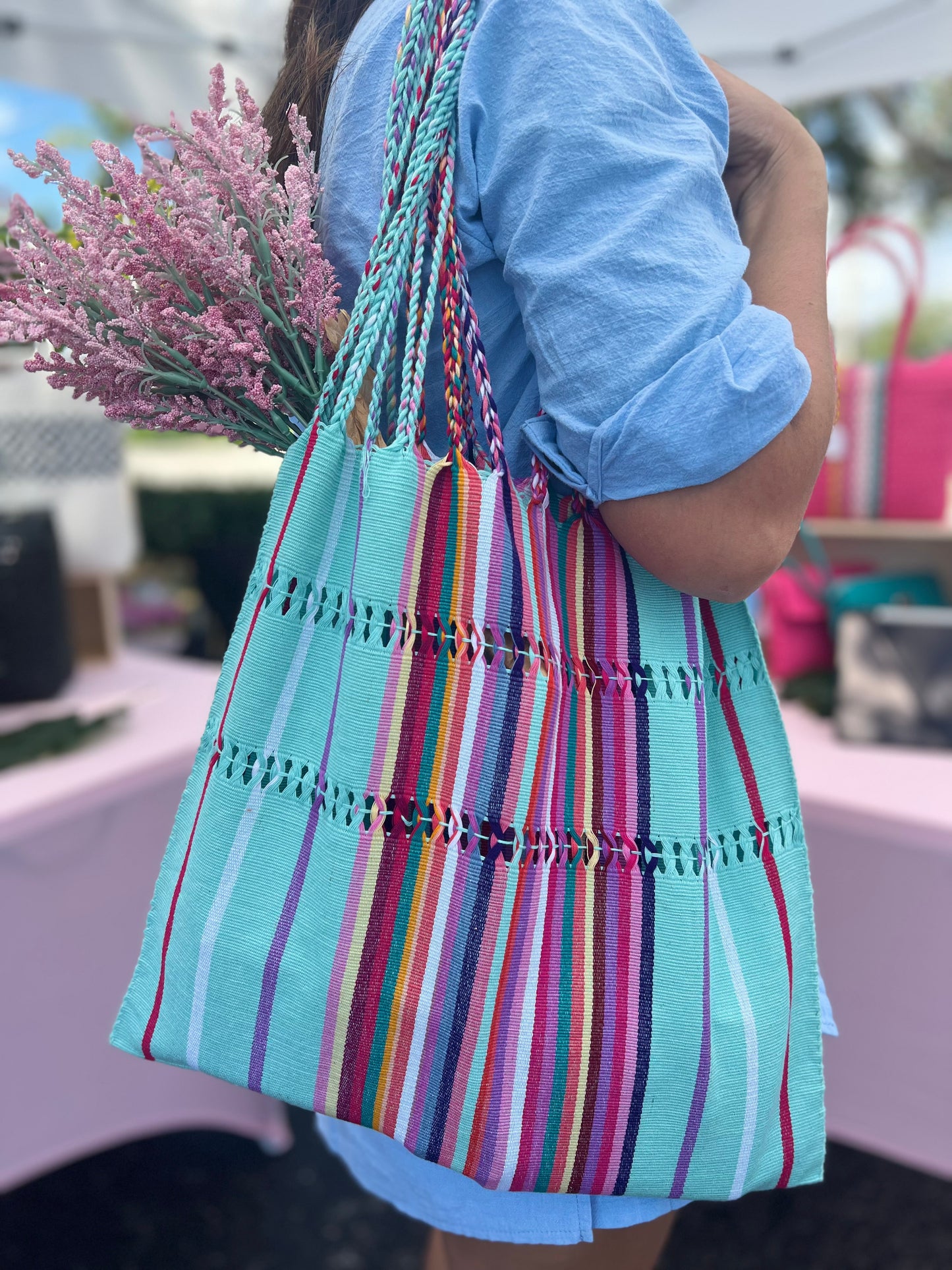 handwoven tote bag with colorful vibrant stripes and intertwined straps. The bag is large and suitable for various uses such as trips to the farmer's market or beach.