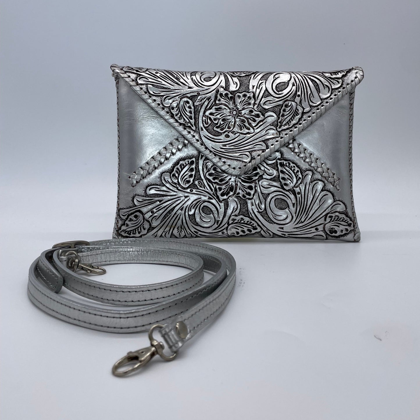 silver crossbody bag with an embossed floral pattern on the flap, featuring a detachable matching strap with metal clasps.