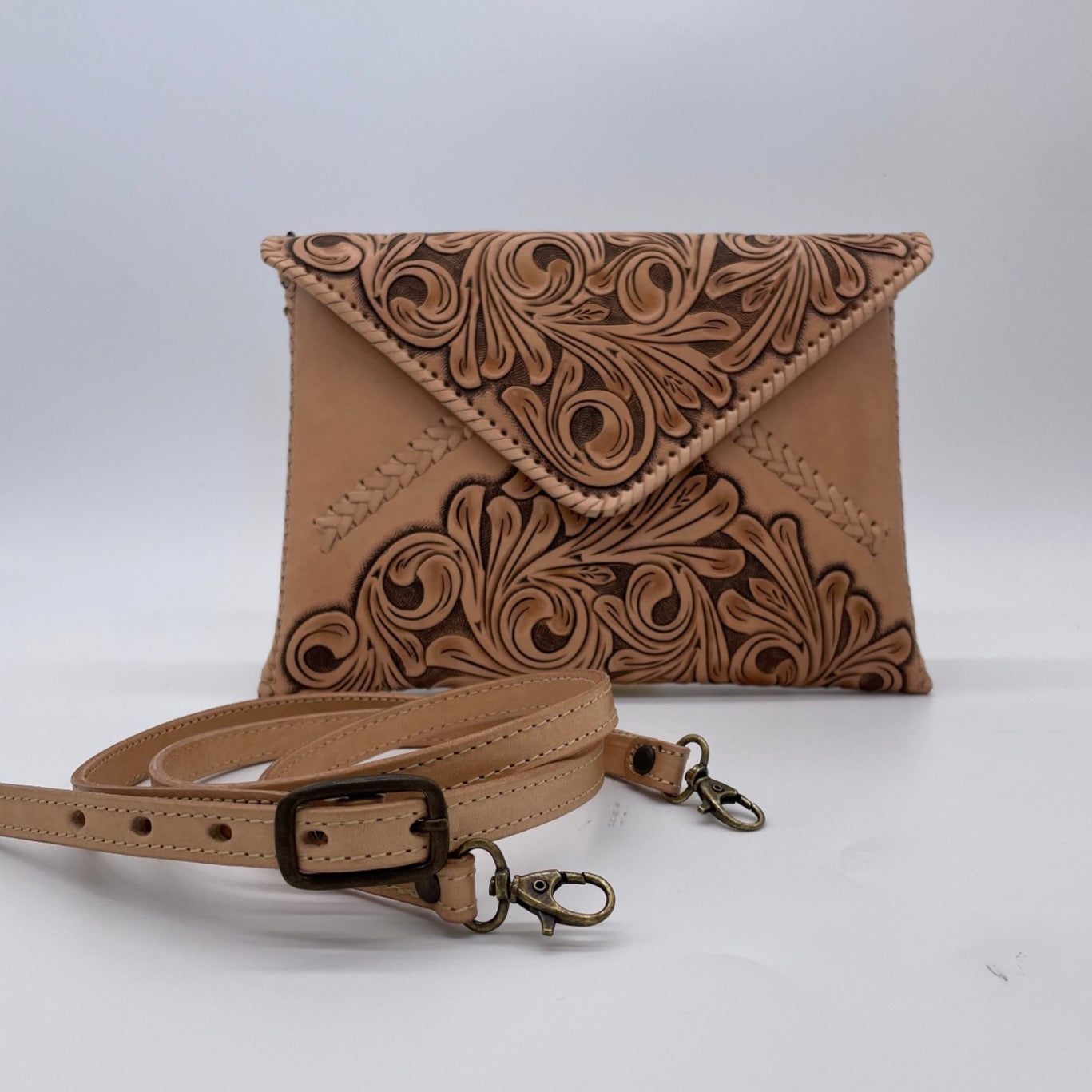 tan crossbody bag with an embossed floral pattern on the flap, accompanied by a detachable strap with metal clasps.