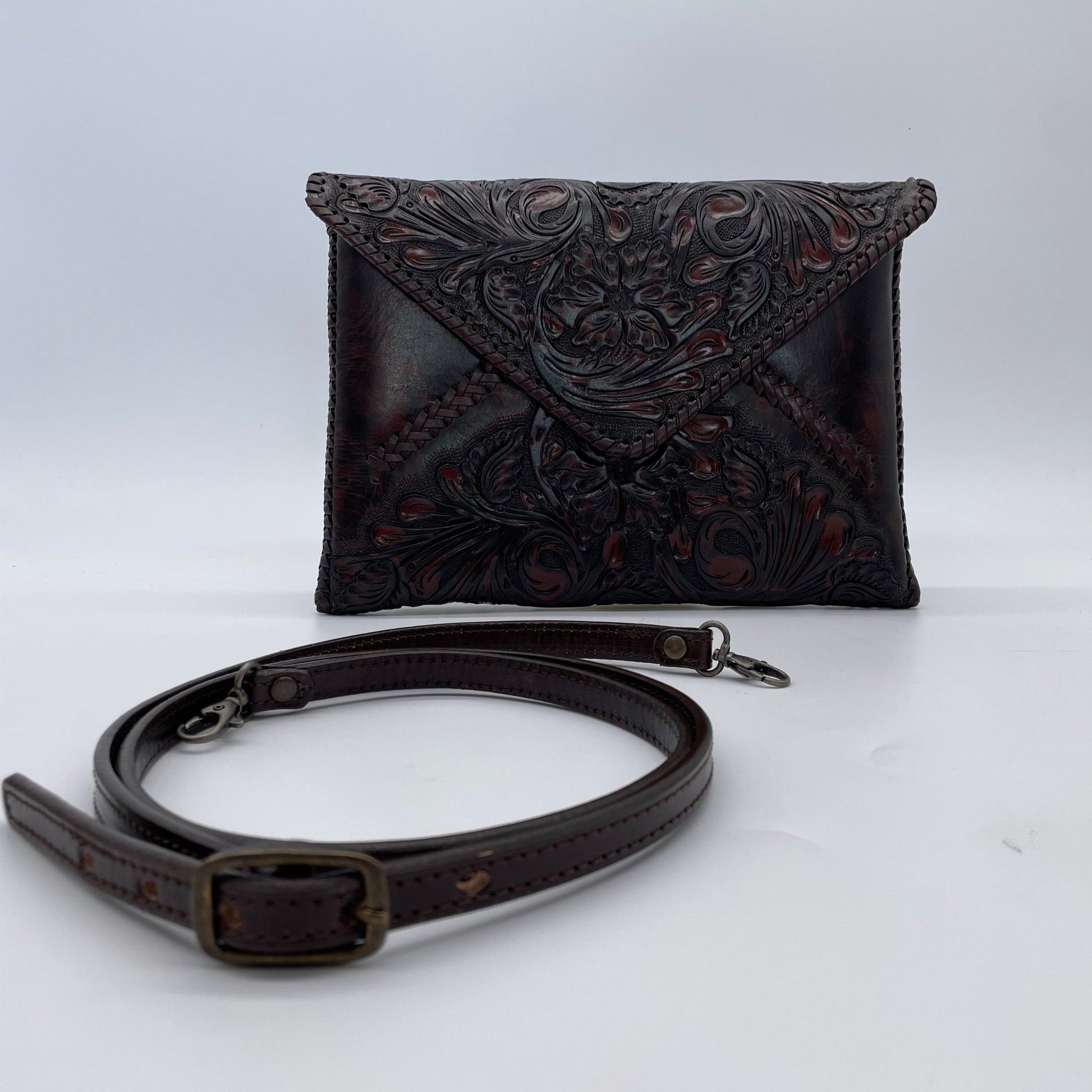 dark brown crossbody bag with an embossed floral pattern on the flap, featuring a detachable matching strap with metal clasps.