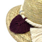 Close-up of a natural fiber hat showing a braided band and tassels in burgundy, white, and gray.