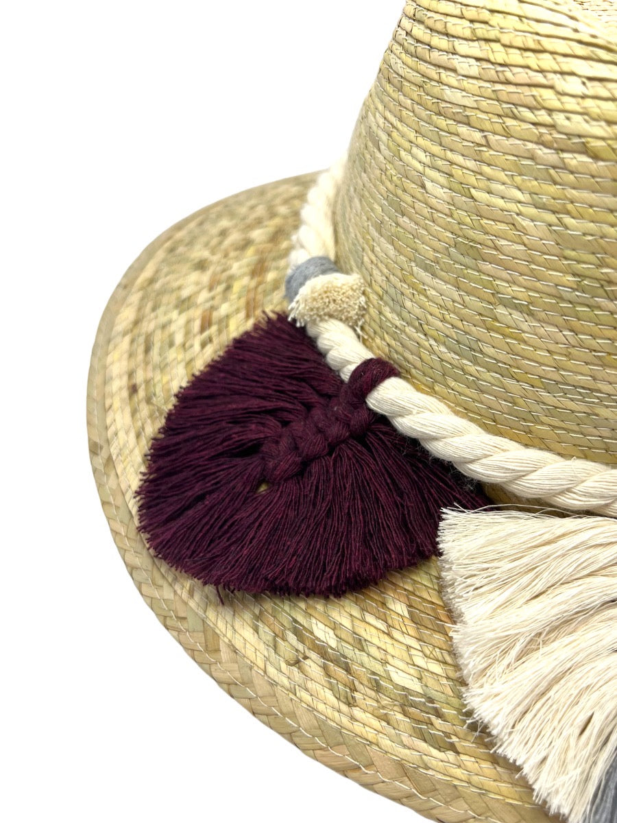 Close-up of a natural fiber hat showing a braided band and tassels in burgundy, white, and gray.