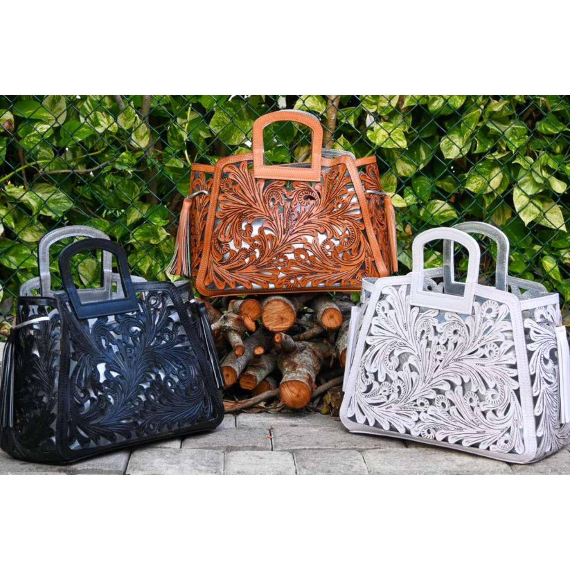 Three handbags with intricate cut-out designs, displayed outdoors. The colors are black, honey, and white, each featuring a rectangular handle and leather tassels on the sides.