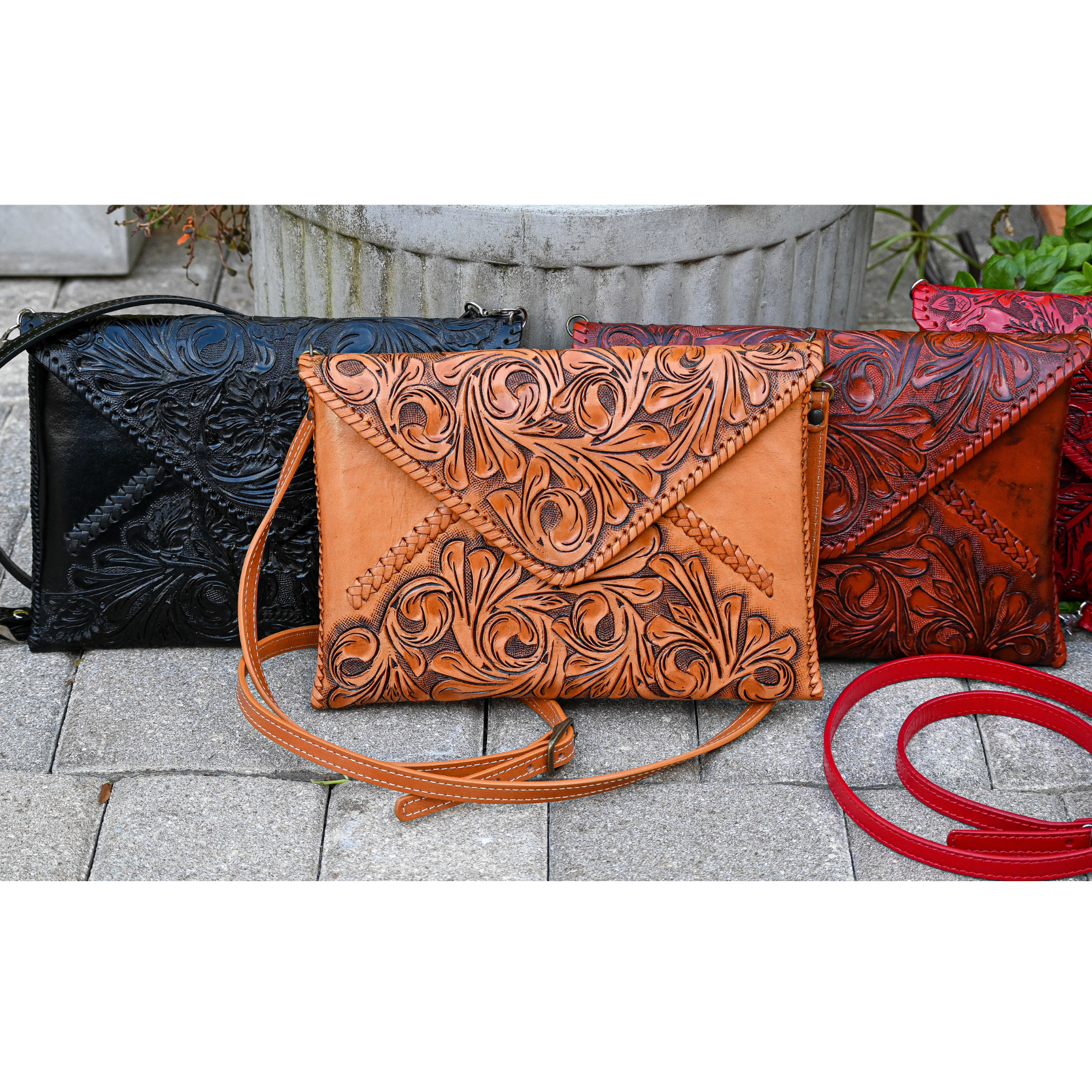 group of crossbody bags in black, honey, and burgundy with intricate embossed floral patterns, displayed together on a stone surface.