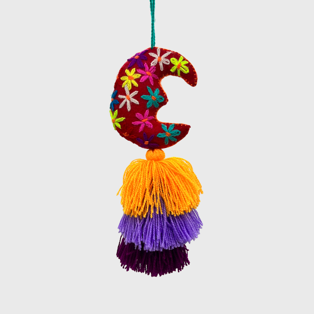 decorative hanging ornament featuring a red crescent moon adorned with colorful embroidered flowers, and three layered tassels in yellow, purple, and dark purple.