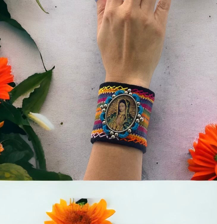 bracelet is decorated with vibrant, textured threads and features a central framed image of The Virgin Mary. It is secured with two magnetic snaps.