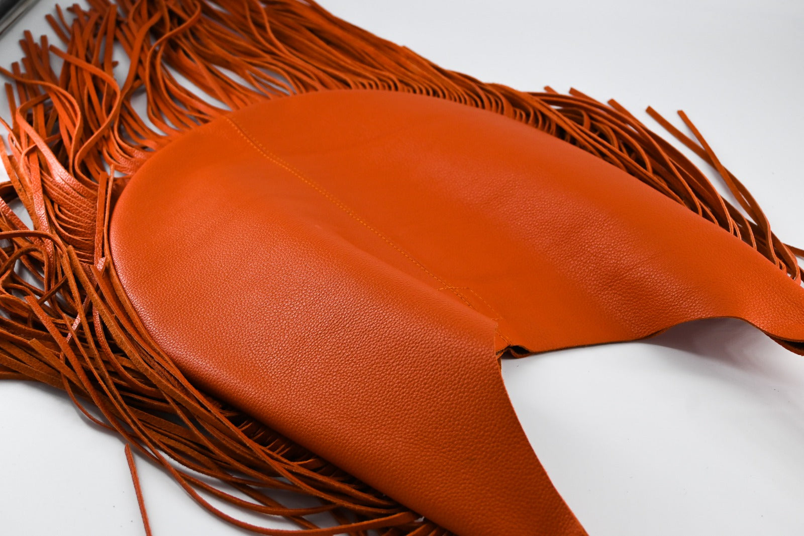 bright orange leather bag with long, flowing fringe details along the sides and bottom.