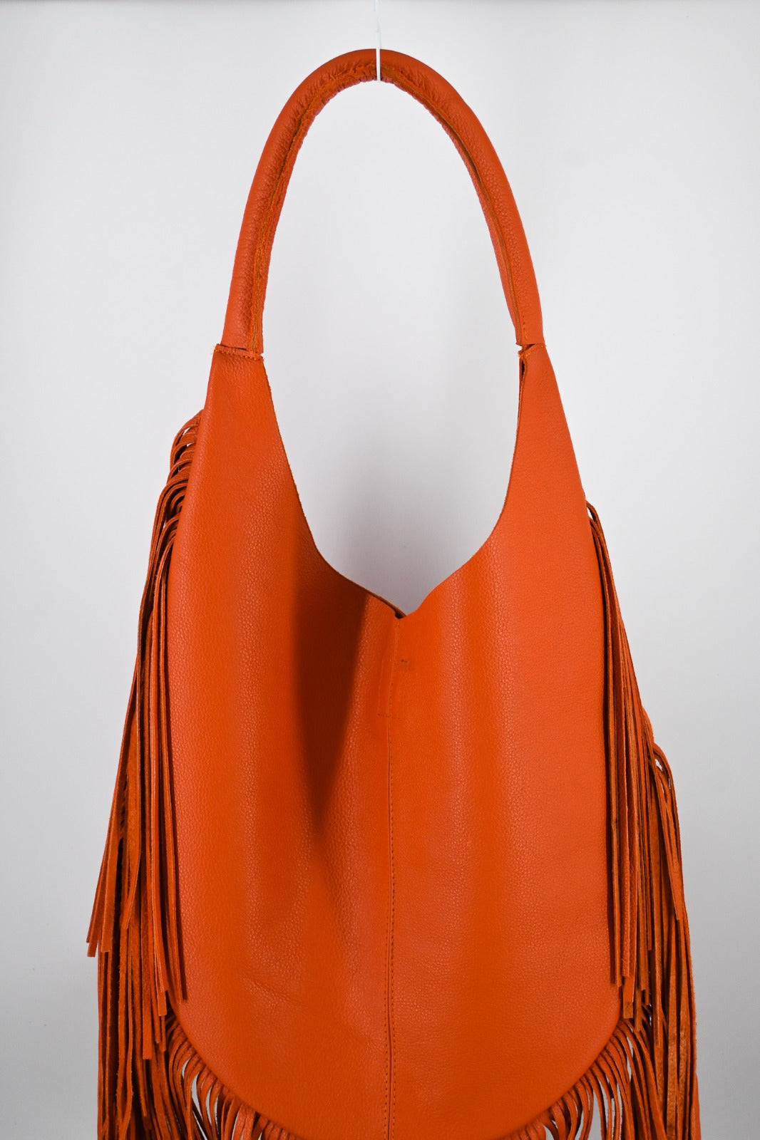 bright orange leather bag with long, flowing fringe details along the sides and bottom.