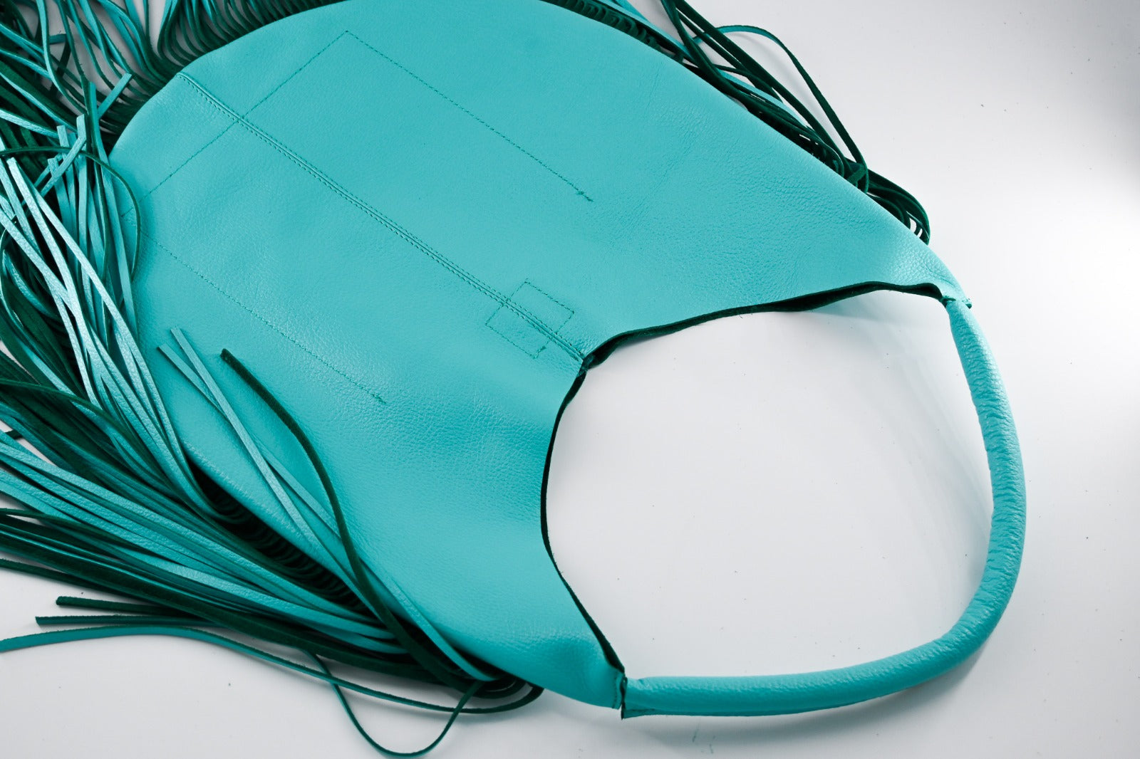 turquoise leather bag with long fringe details along the sides and bottom, featuring a padded wrapped shoulder strap.