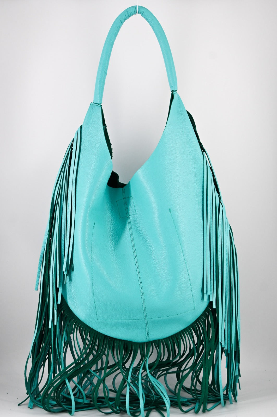 turquoise leather bag with long fringe details along the sides and bottom, featuring a padded wrapped shoulder strap.