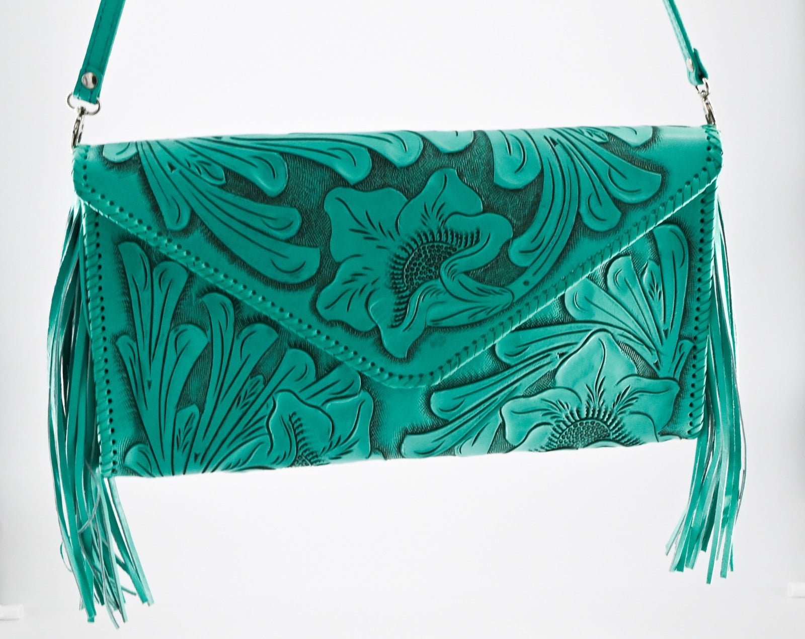 turquoise leather clutch with intricate floral carvings, long side tassels, and a matching strap. It has a snap front closure.
