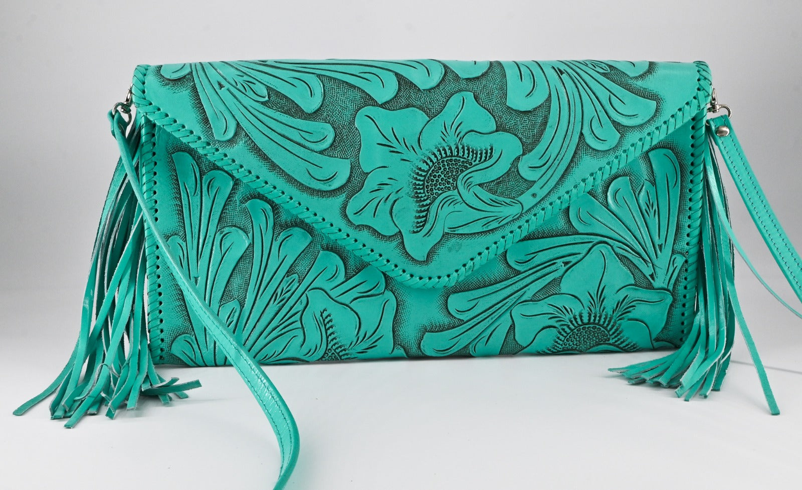 turquoise leather clutch with intricate floral carvings, long side tassels, and a matching strap. It has a snap front closure.