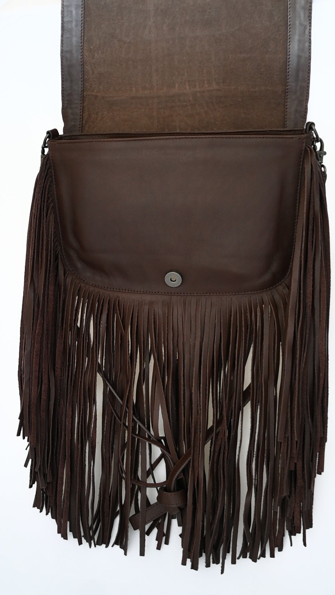 brown leather crossbody bag with long fringe and an open flap. The inside of the bag is visible, showing a magnetic button closure.