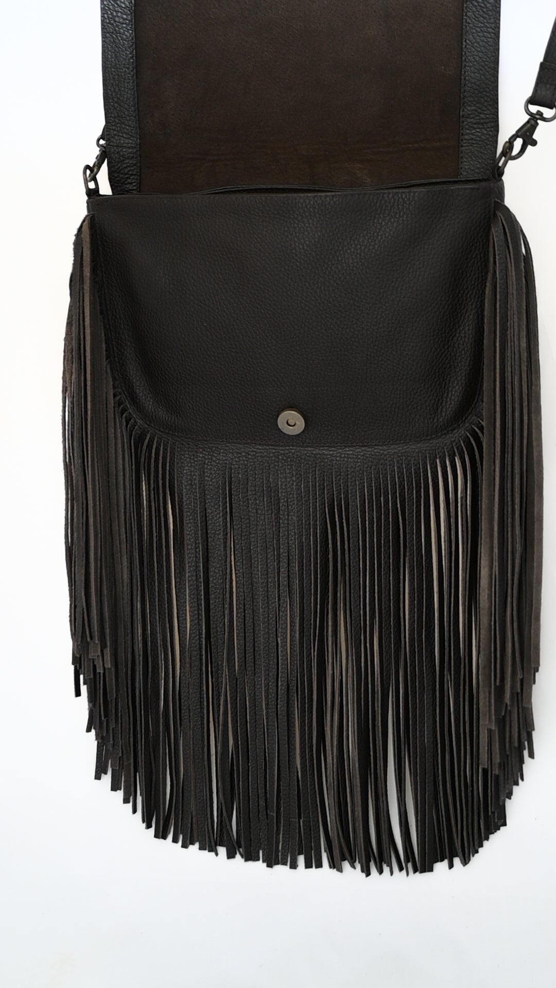 black leather crossbody bag with long fringe and an open flap. The inside of the bag is visible, showing a magnetic button closure.